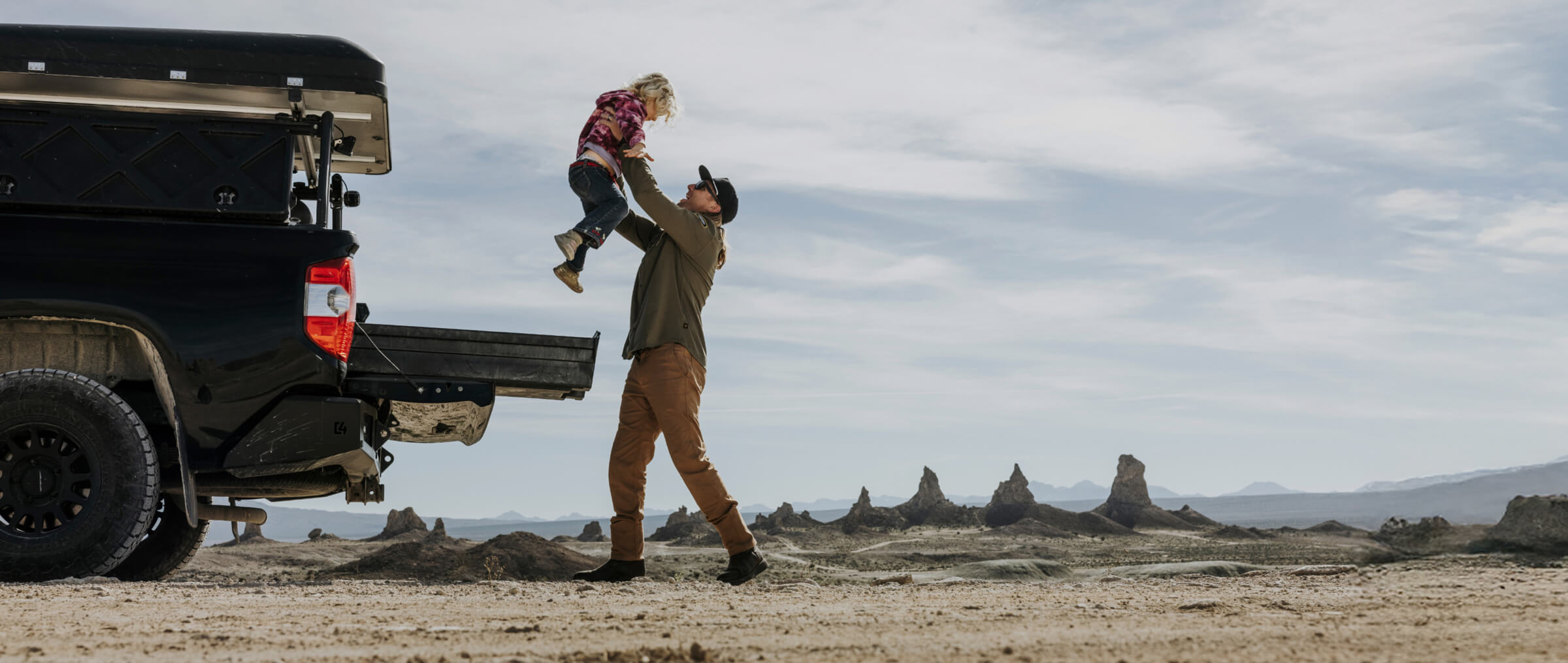 A dad tossing his little girl into the air while they are camping in the desert with a truck, rooftop tent, and DECKED Drawer System!