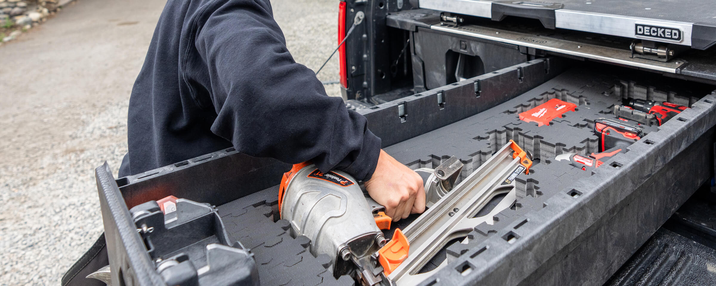 A man grabbing a nail gun that is stored safely in the Drawer of a DECKED Drawer System's Piecekeeper PuzzleFoam.