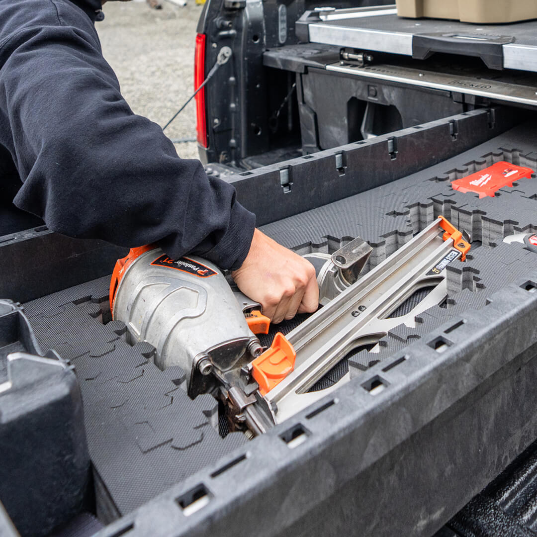 A man grabbing a nail gun that is stored safely in the Drawer of a DECKED Drawer System's Piecekeeper PuzzleFoam.