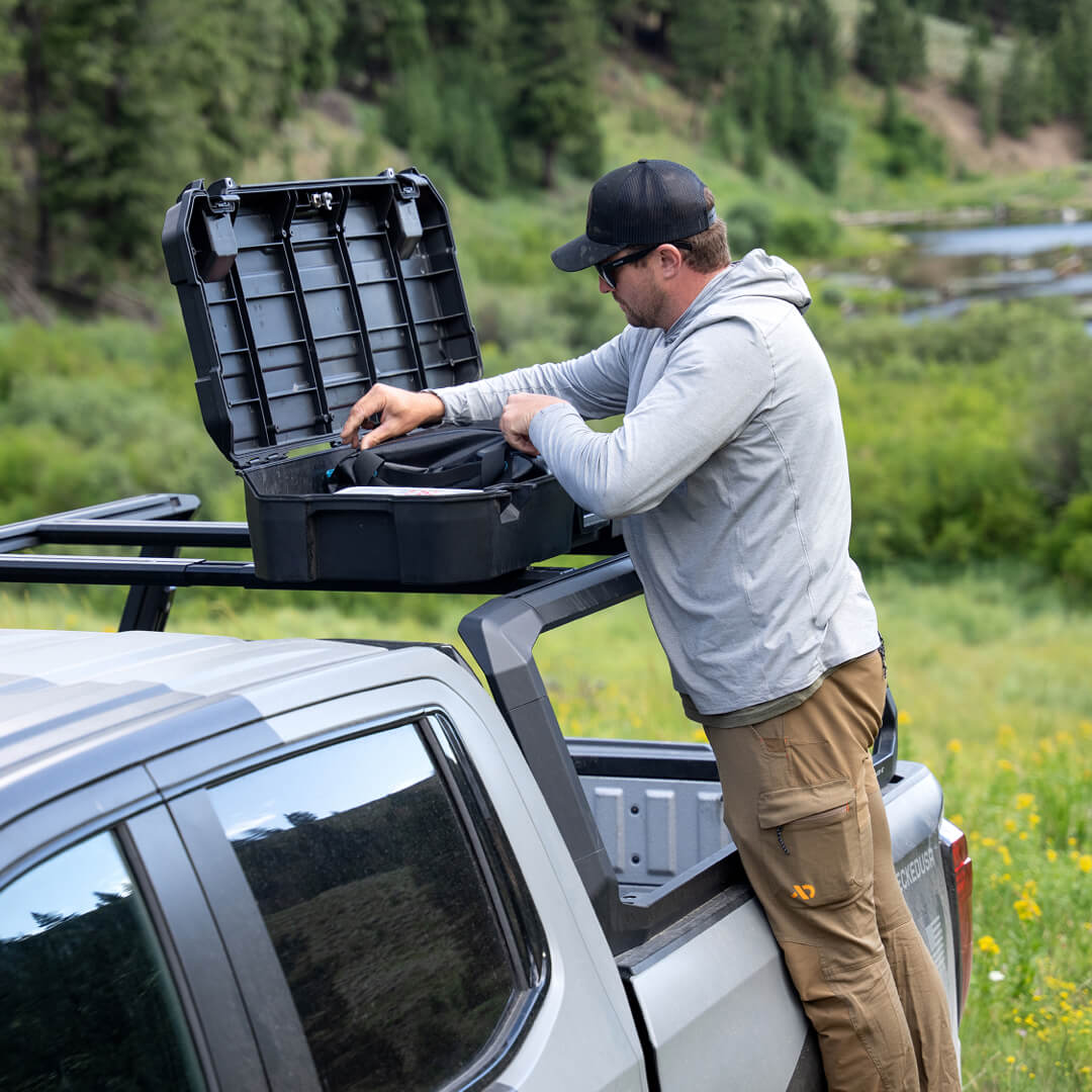 A man grabbing gear from the Honcho D-co case that is mounted to his truck's roof rack.