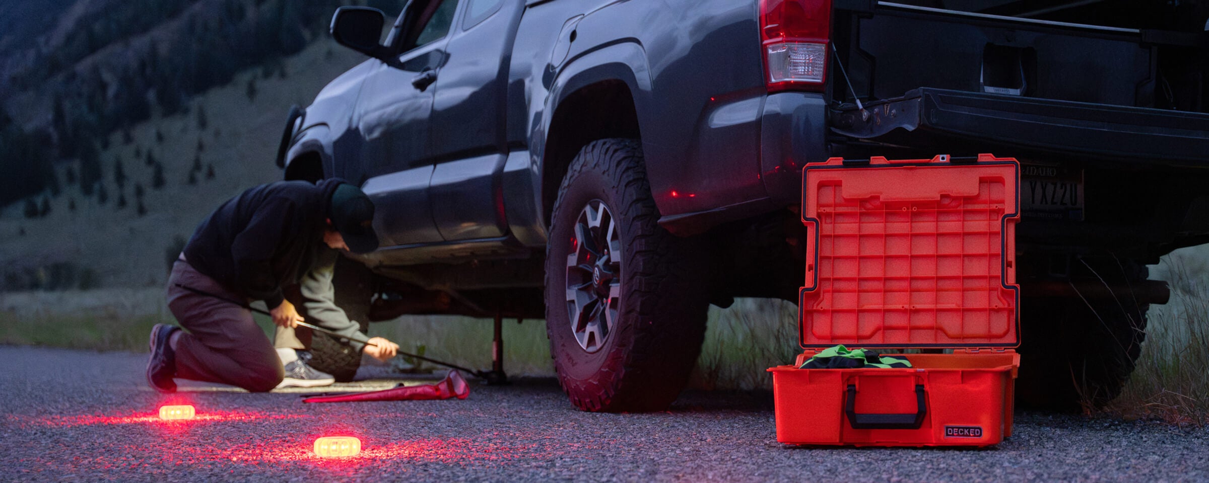 A man jacking his car up to change his tire with his LED flares and Roadside Emergency Kit close by.