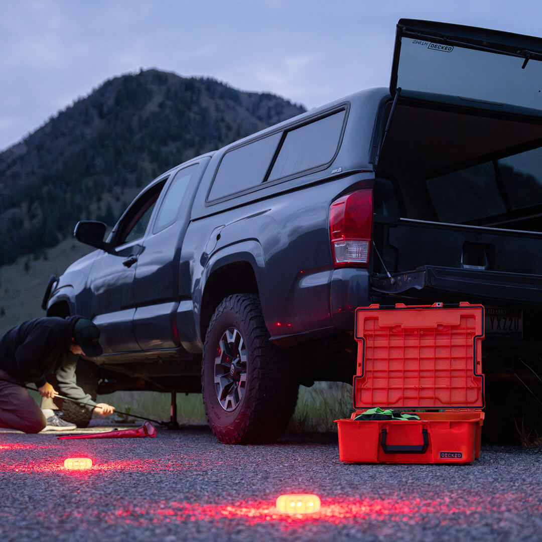 A man jacking his car up to change his tire with his LED flares and Roadside Emergency Kit close by.