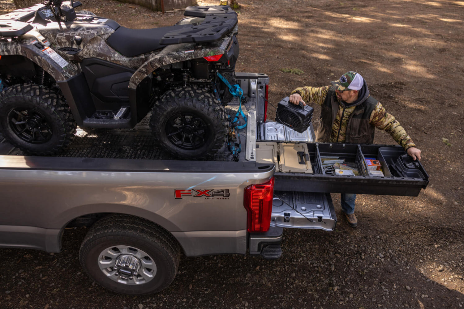 A man retrieving a Turtlebox speaker from his DECKED Drawer System. He has an ATV securely strapped to the deck of his Drawer System.