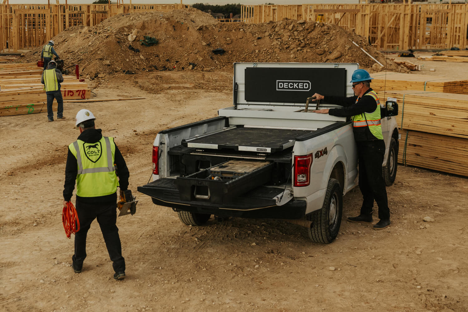 Construction workers loading a d-co case into an open white toolbox with a drawer system and CargoGlide mounted on top in a truck bed.
