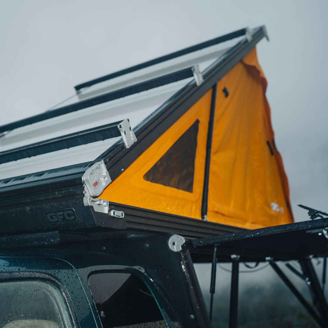 Orange rooftop tent attached to a vehicle with a gray background