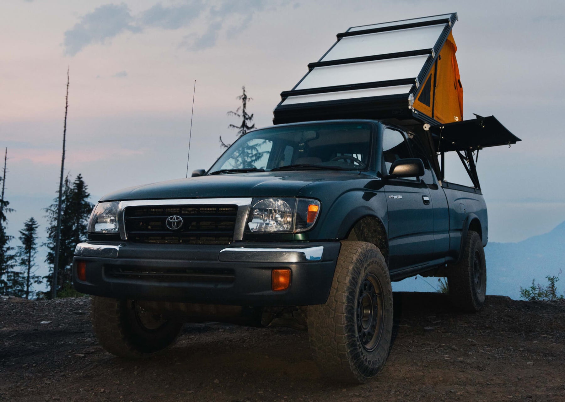Blue Toyota truck with a camper shell in a mountainous area