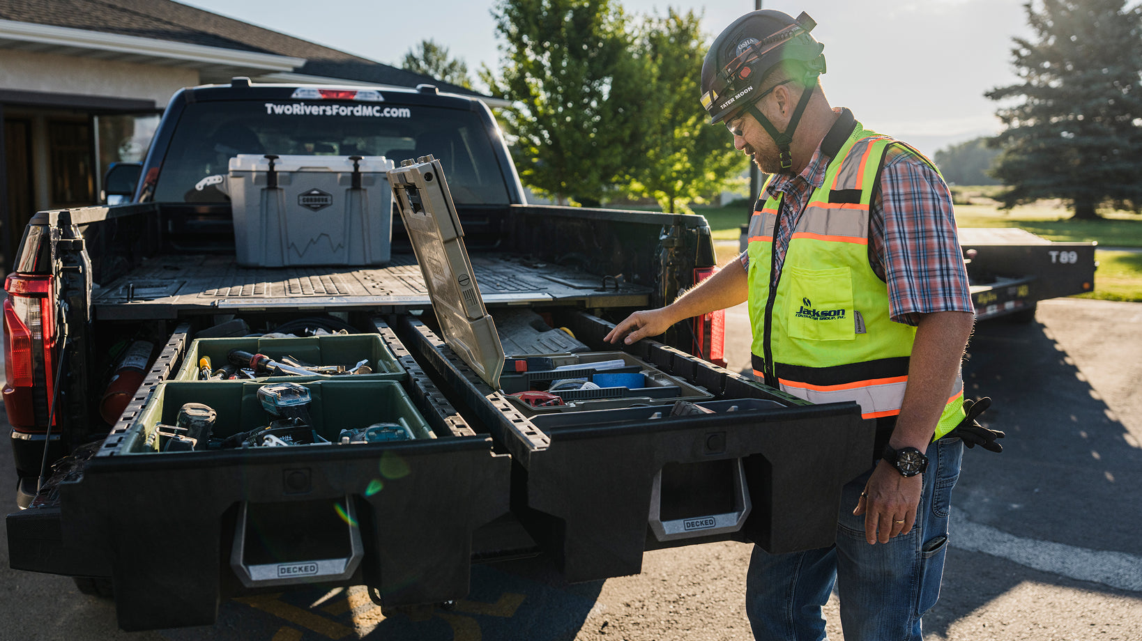 Construction worker accessing organized tools from open DECKED drawers in a pickup truck bed.