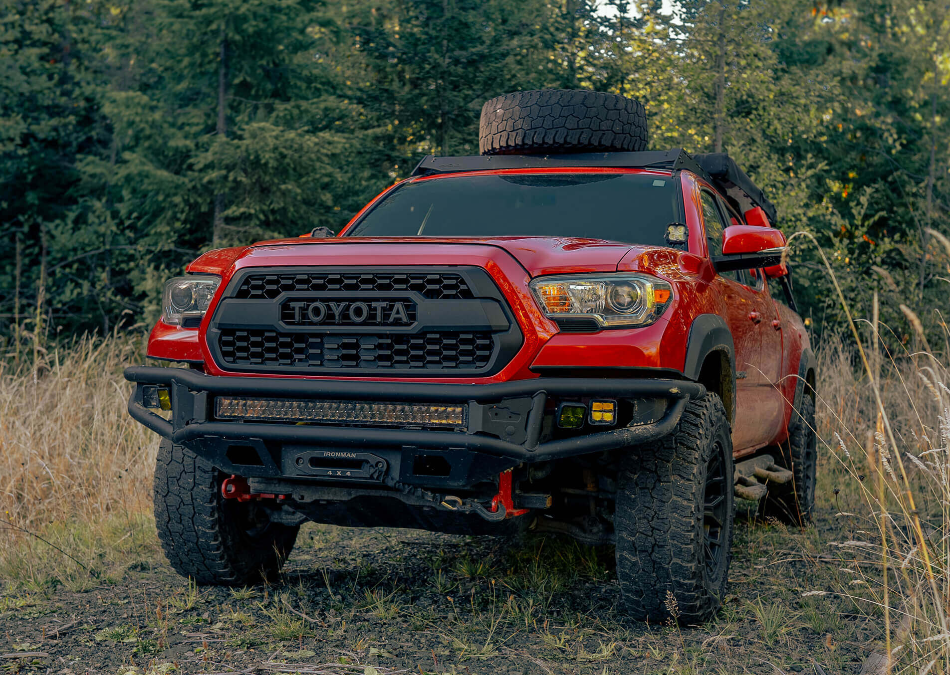 Red Toyota truck with off-road tires in a forest setting