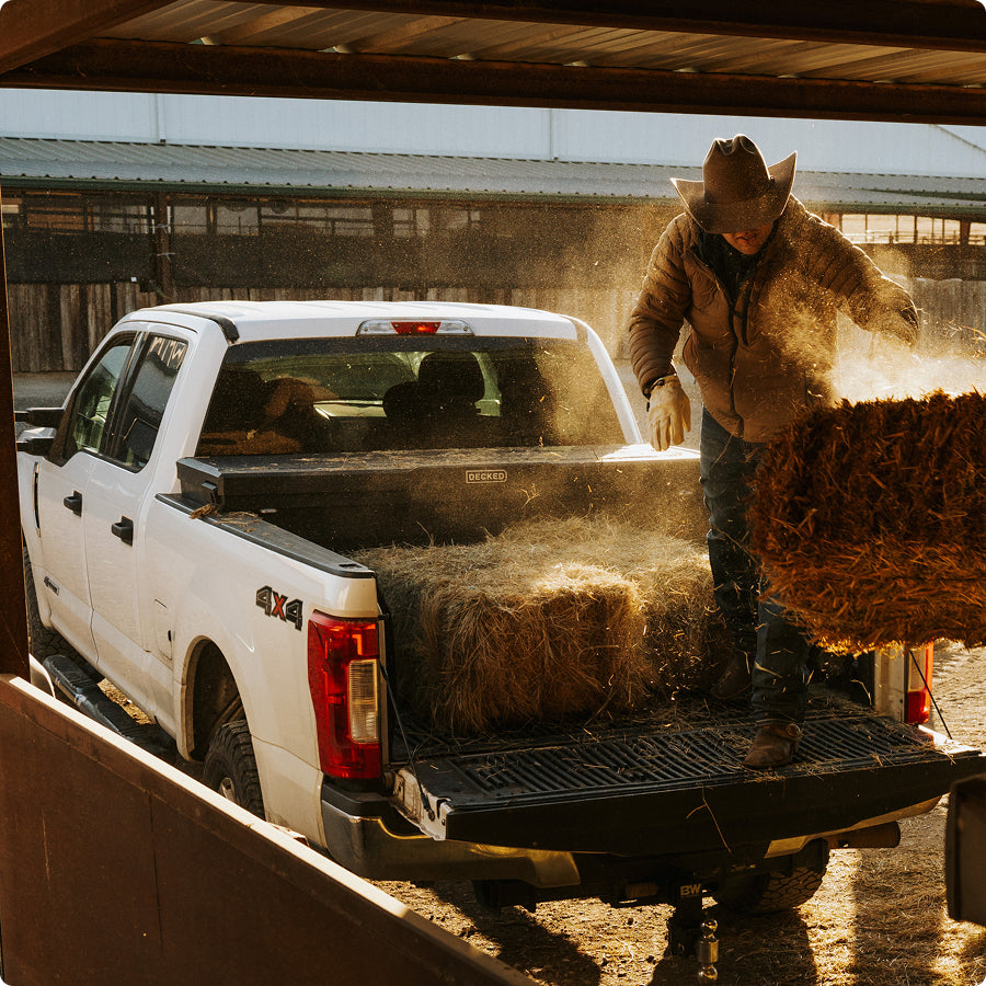 Rancher unloading hay bales from a pickup truck equipped with a DECKED Tool Box.