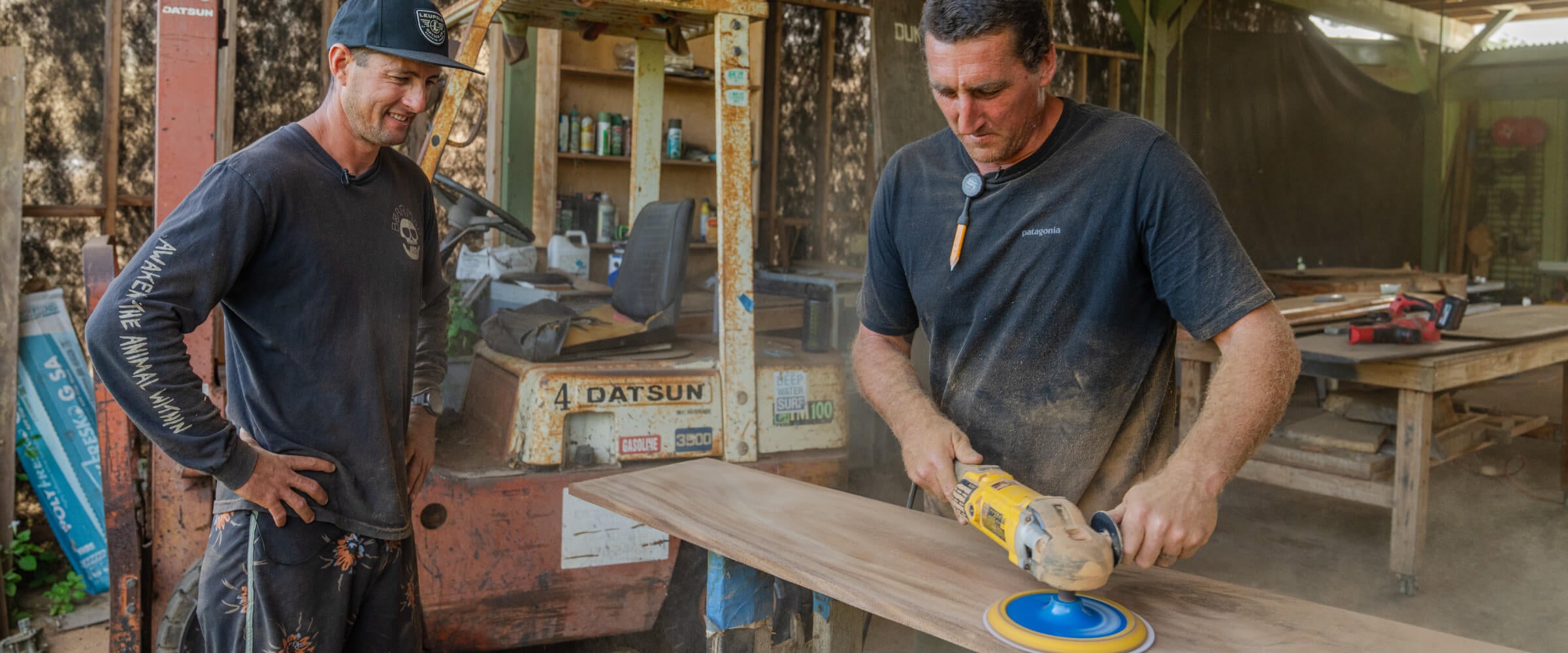 Two men working with a power tool in an outdoor workshop setting.