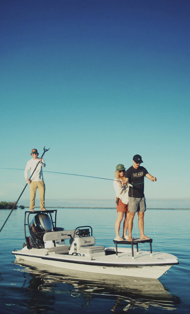 Four people on a small boat in calm water with a clear blue sky.