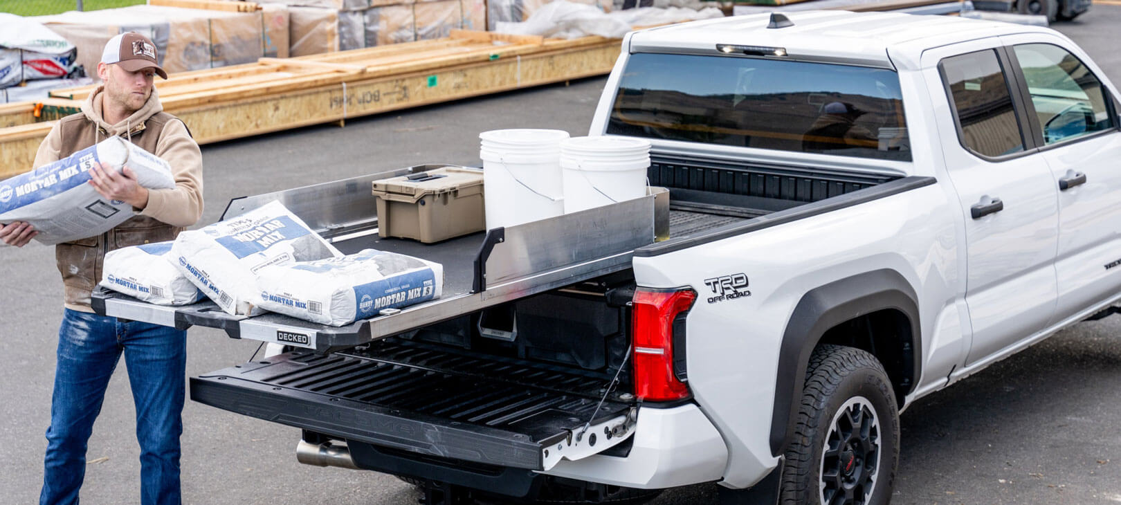 A man loading 80lb mortar mix onto a CargoGlide mounted on a Drawer System in a midsize truck.