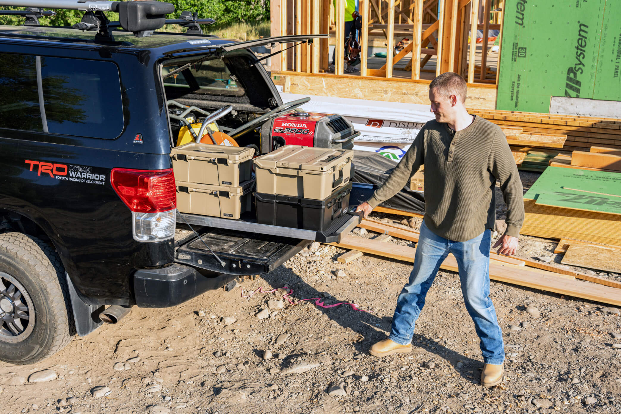 A man at a construction site pulling his CargoGlide, stacked with D-co Cases and other equipment out of his truck bed.