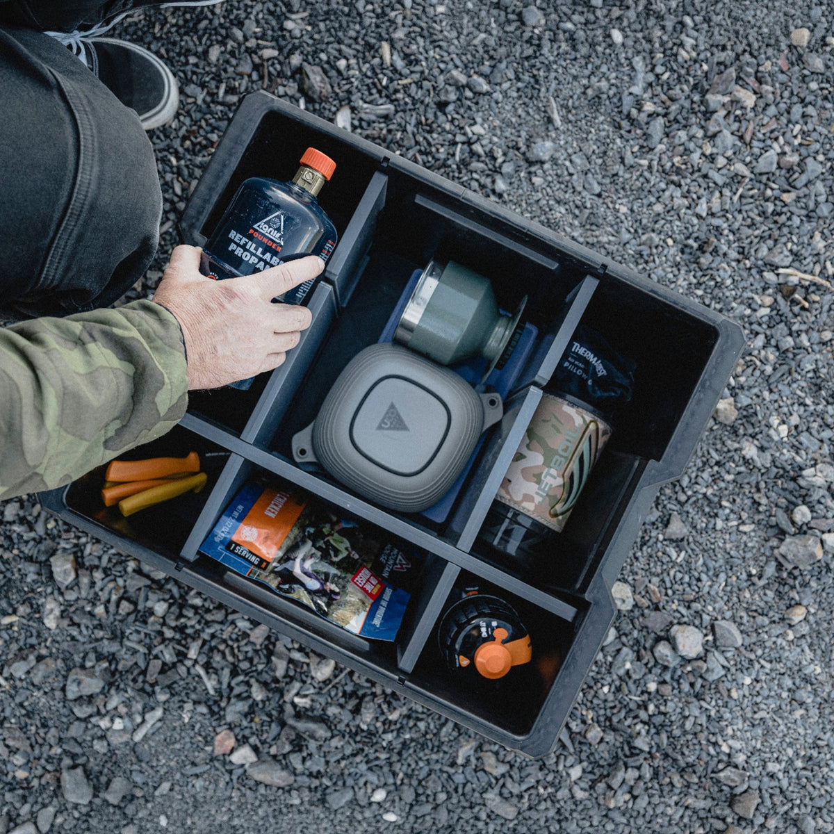 Person organizing camping cookware, fuel, food, and accessories in a DECKED Payloader using the customizable POD divider system.