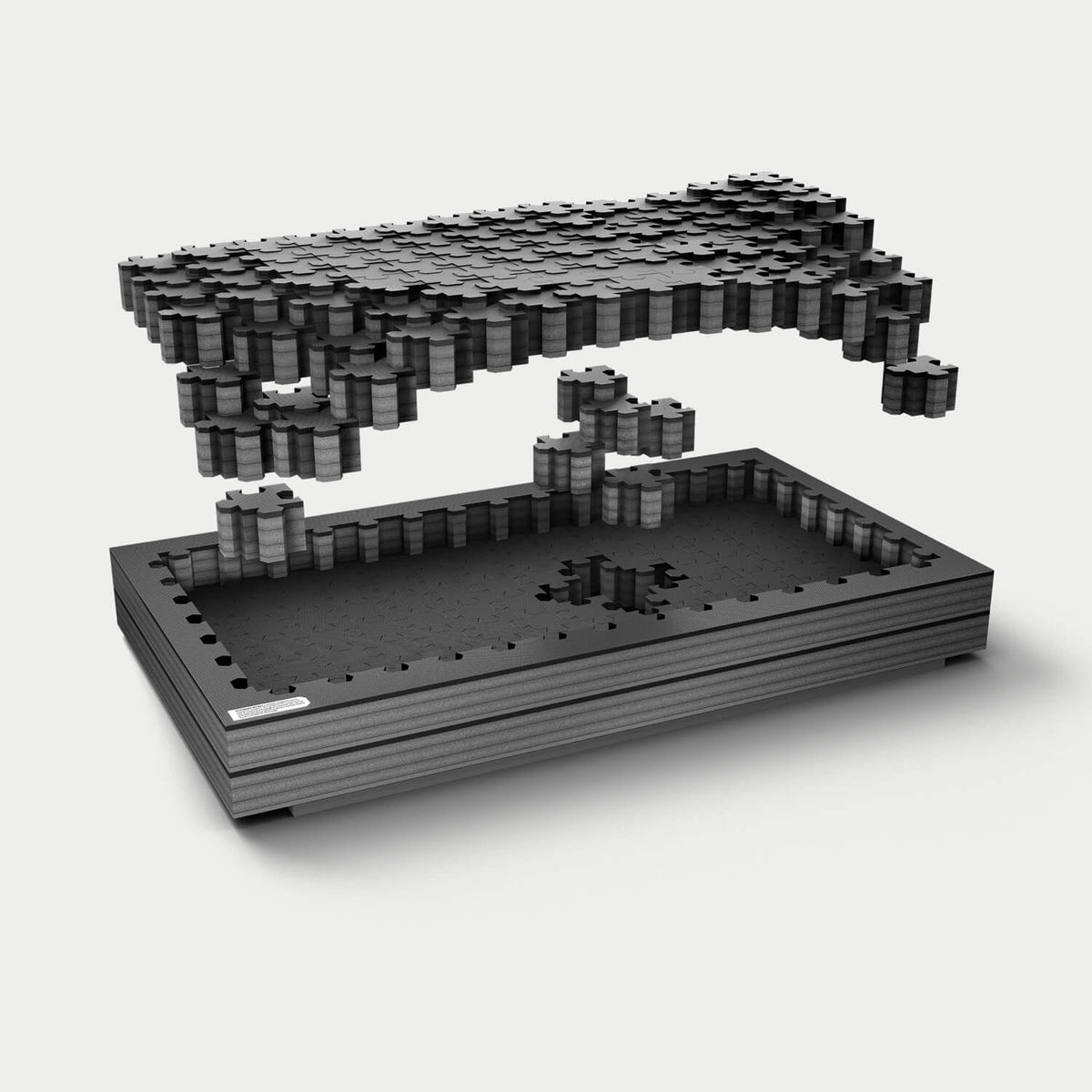 Exploded view of DECKED puzzle foam layers rising above a base tray, showing interlocking gray foam pieces with a custom pull-out section removed to create a storage cavity.