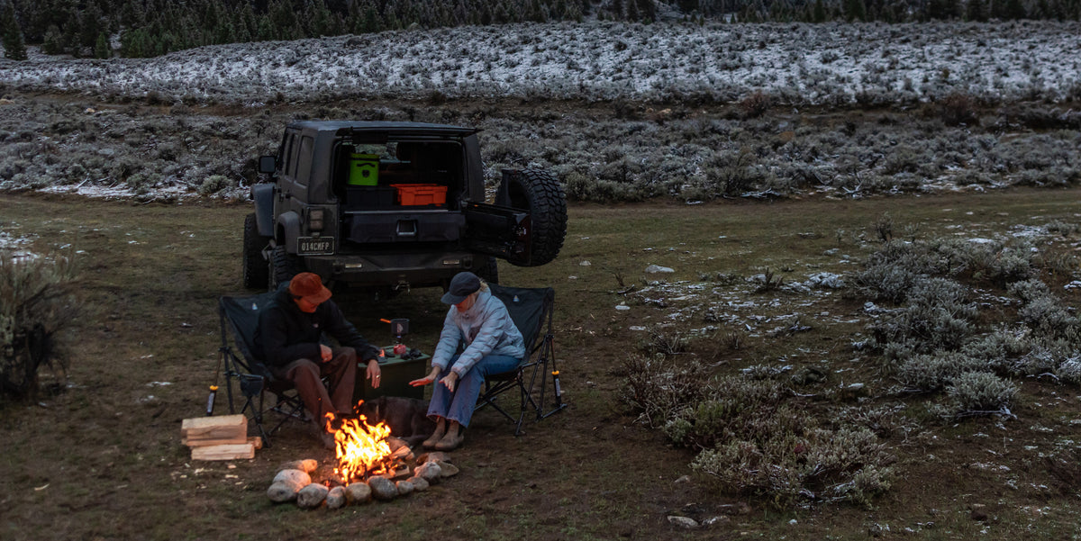 Two people sitting by a campfire behind a Jeep Wrangler with a DECKED Drawer System.