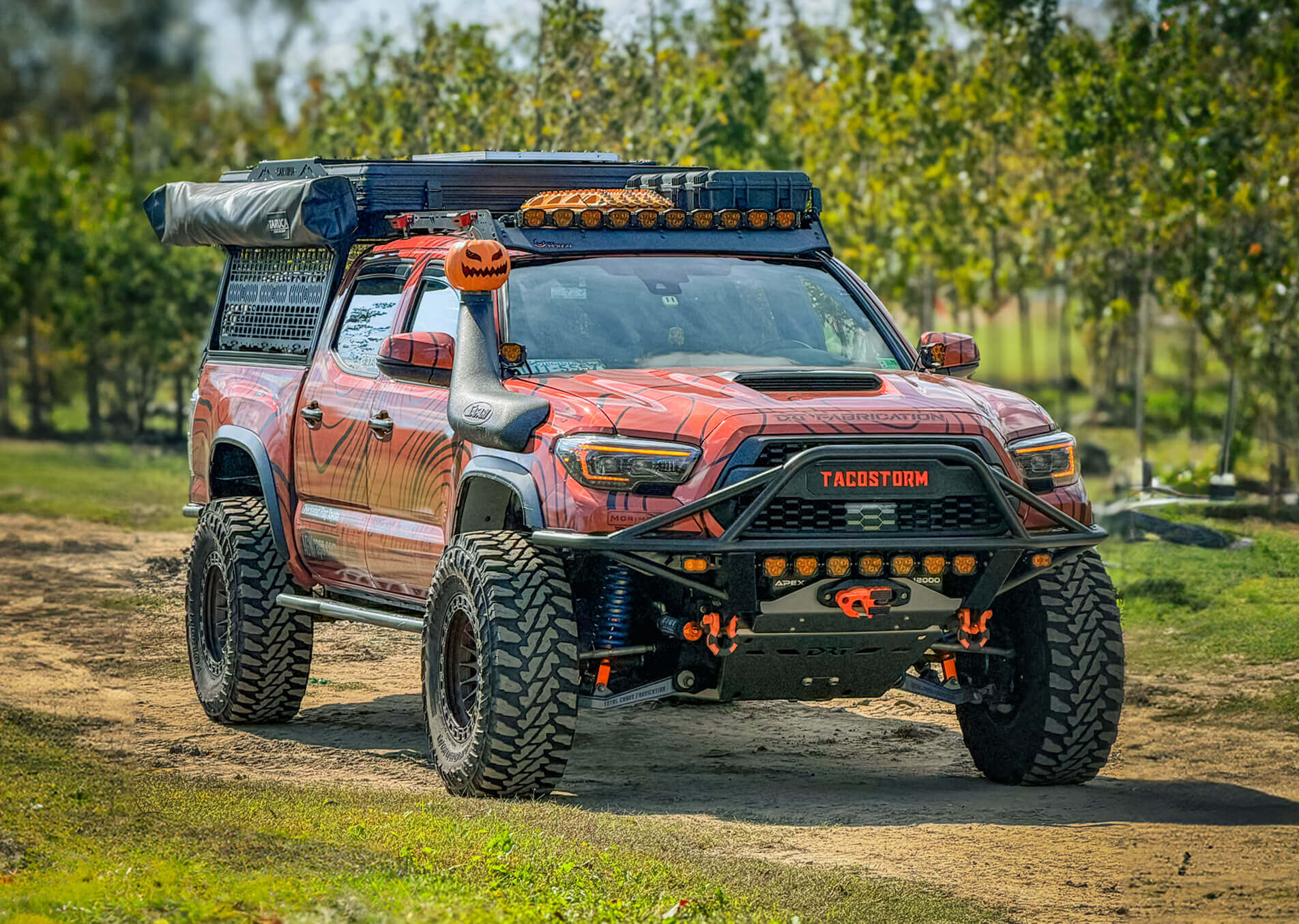 Red off-road truck with additional lights and equipment on a dirt road.