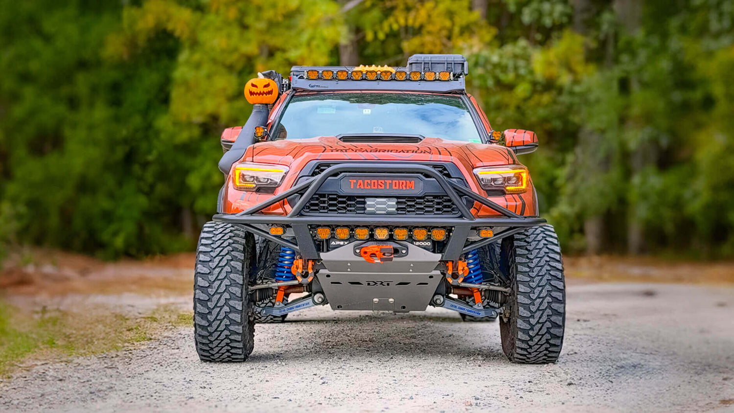 Orange off-road vehicle with large tires on a dirt road surrounded by greenery