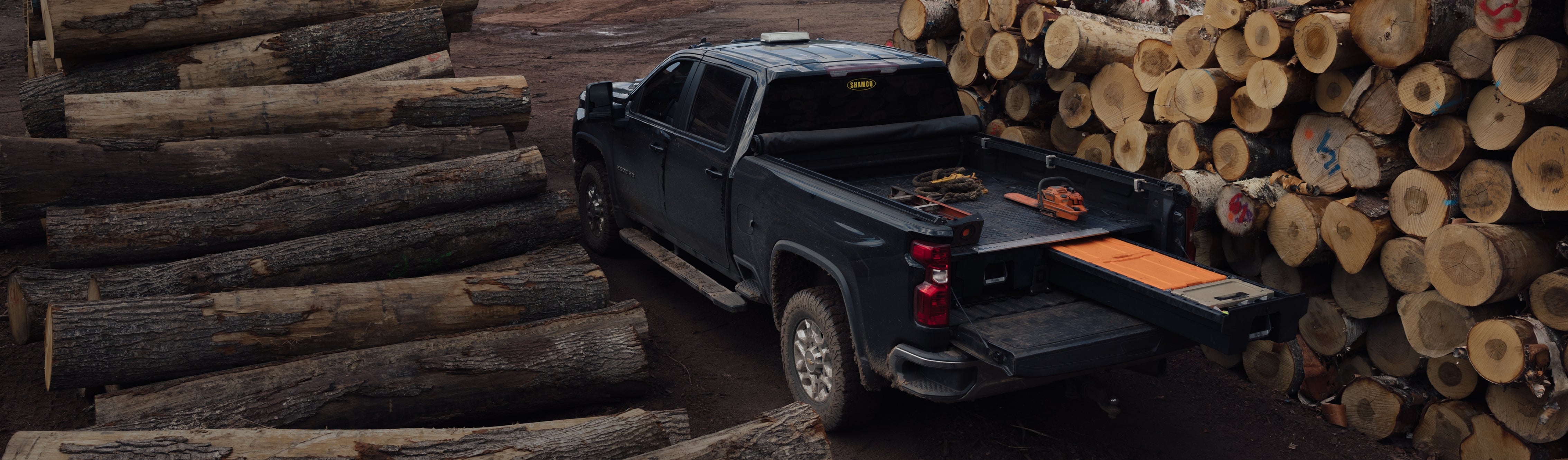 DECKED Drawer System open in a pickup truck bed surrounded by stacks of timber at a logging site.