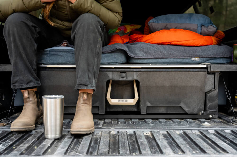 Person sitting in a truck bed with camping gear and a tumbler.