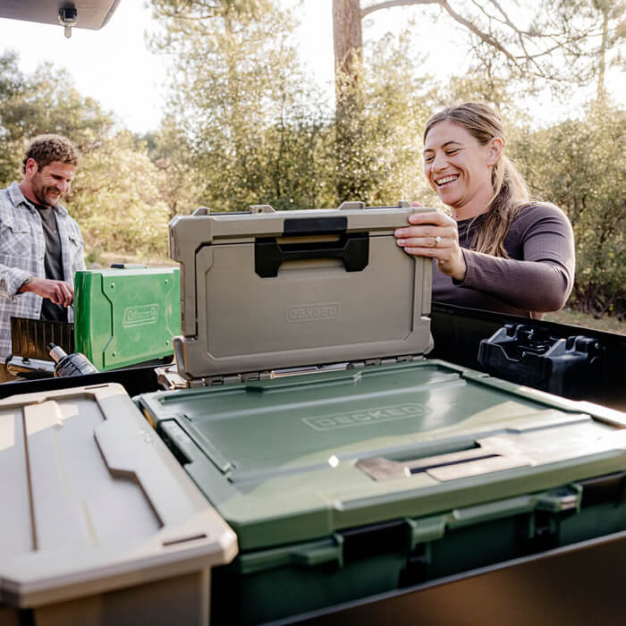 Two people grabbing camp kitchen supplies out of their with DECKED D-co storage cases.