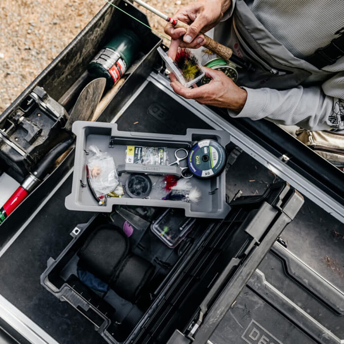 Open Sixer 16 tool box with various tools and equipment, person holding a fishing rod.