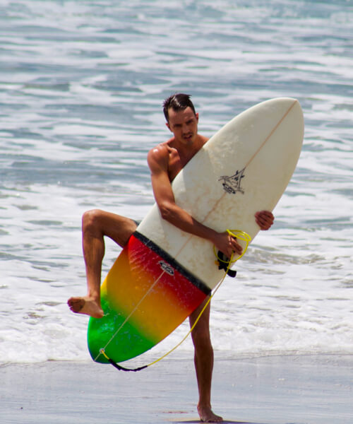 Chis wrestling with his surfboard on the beach.