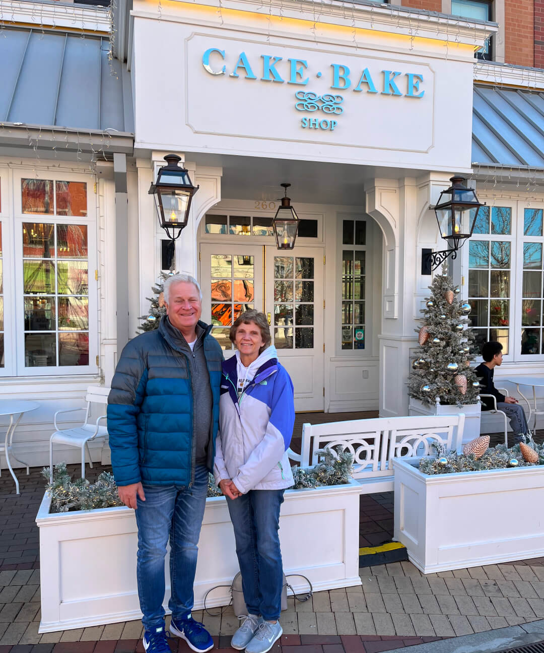 Chuck and his wife smiling in front of a bakery.