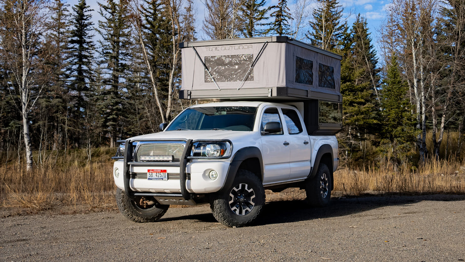White truck with a camper shell parked on a dirt road surrounded by trees.