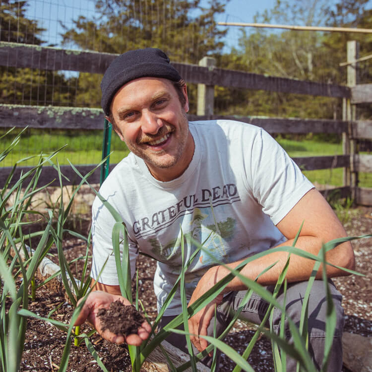 Brad Leone smiling in his garden, holding a handful of dirt towards the camera.