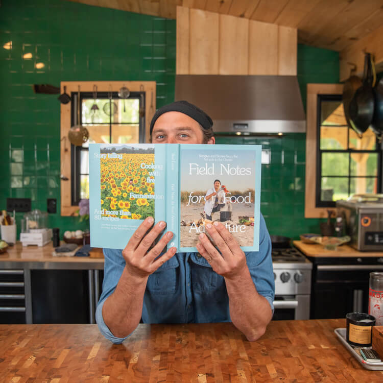 Brad Leone in the kitchen, holding up his book, Field Notes for Food.