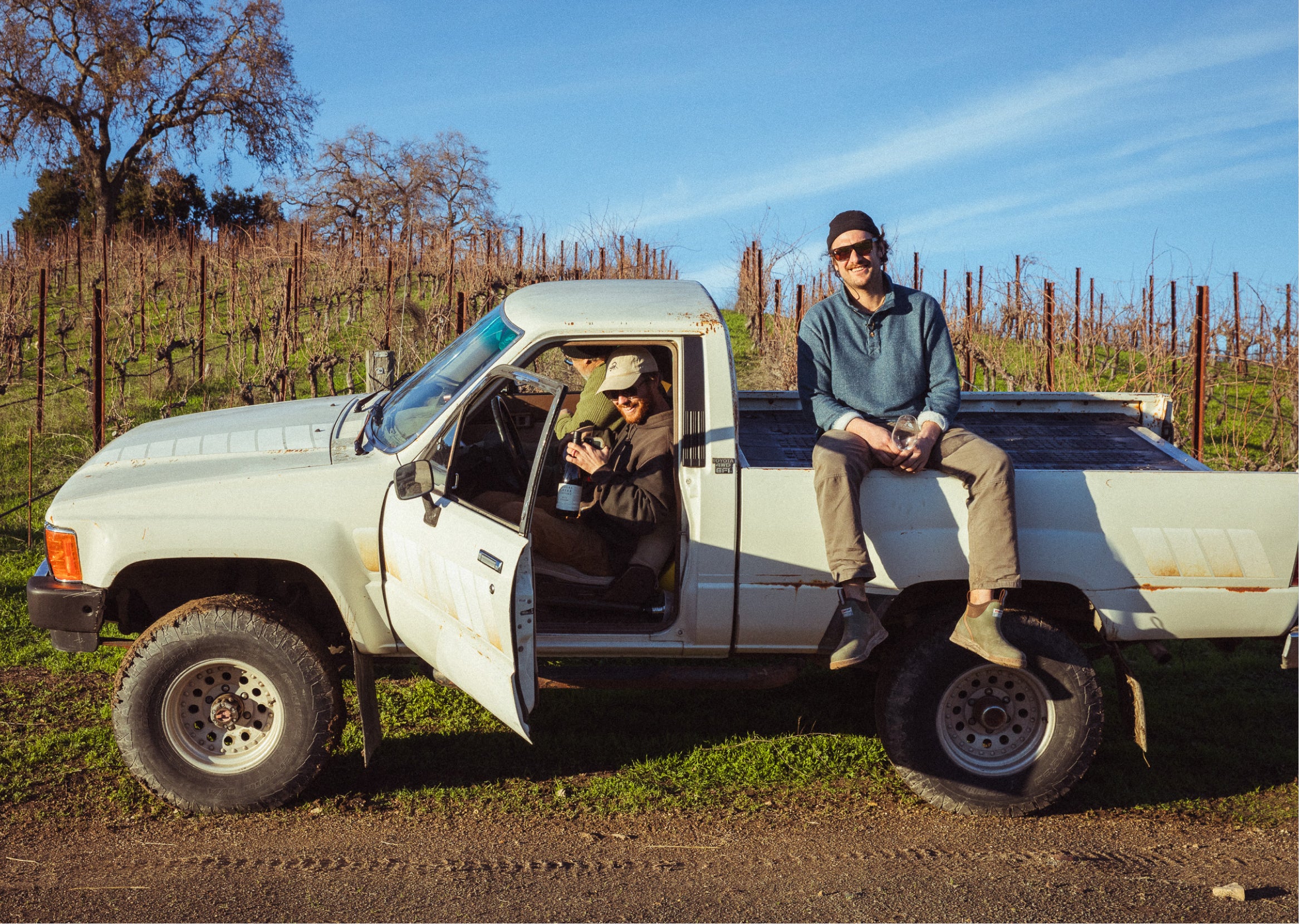 Brad Leone sitting on the side of his truck bed with his friends in the front seats of his truck.