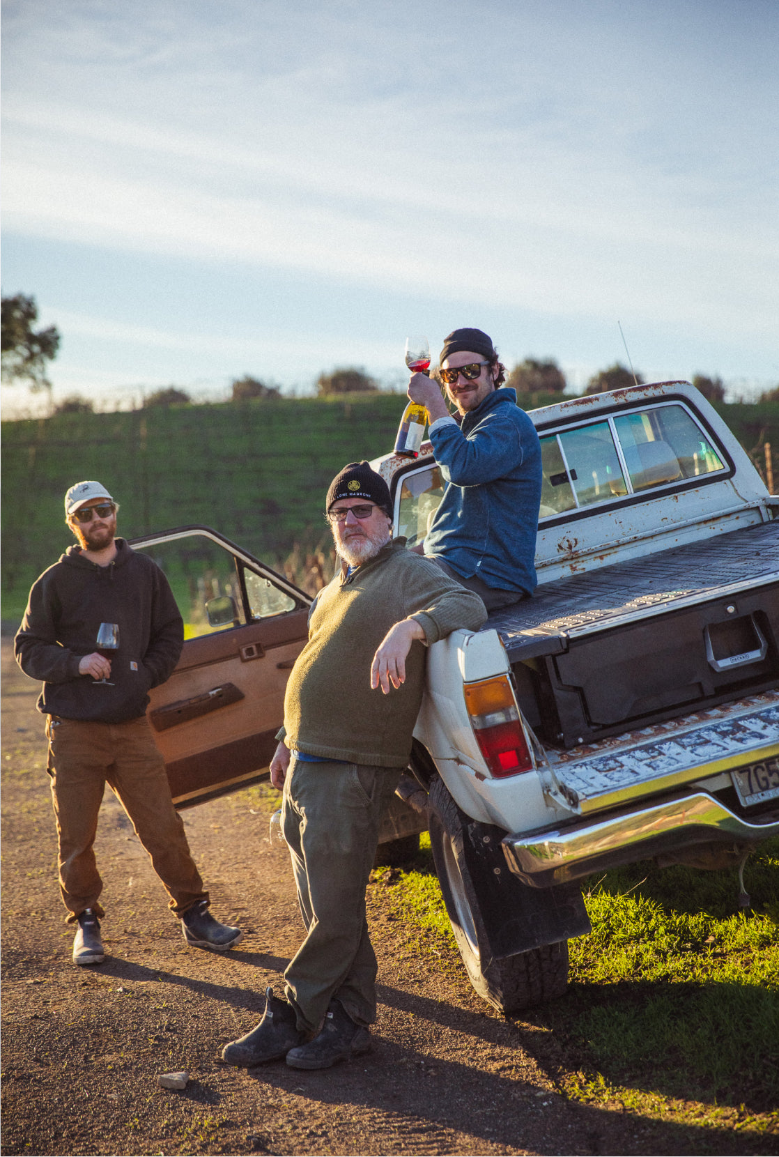 Brad Leone lounging on the side of his truck with a glass of wine and friends in a vineyard.