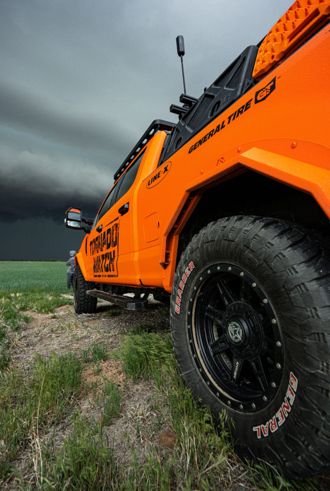 Orange off-road vehicle with large black tires on a grassy path under a cloudy sky.
