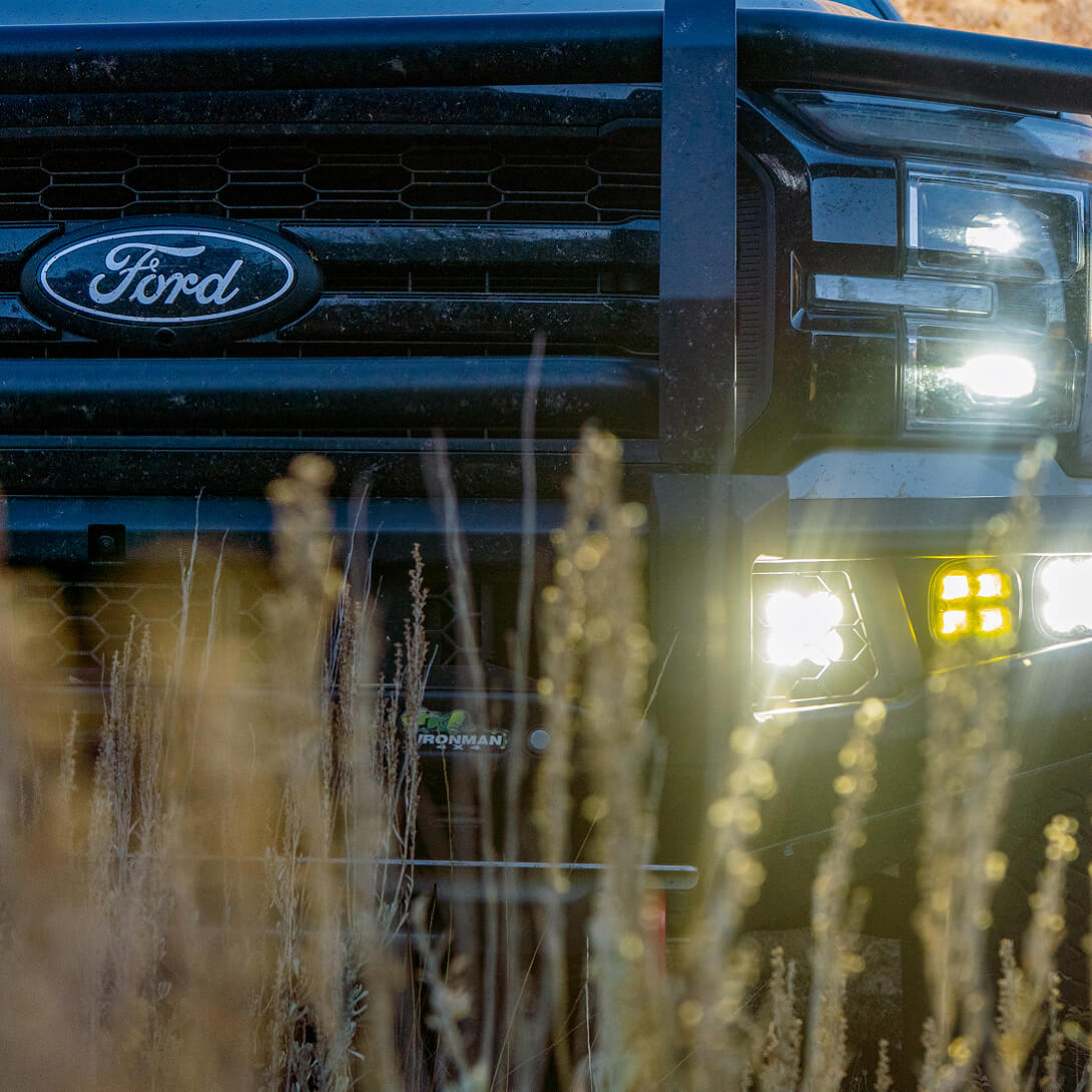 Ford vehicle front with headlights on, surrounded by tall grass.