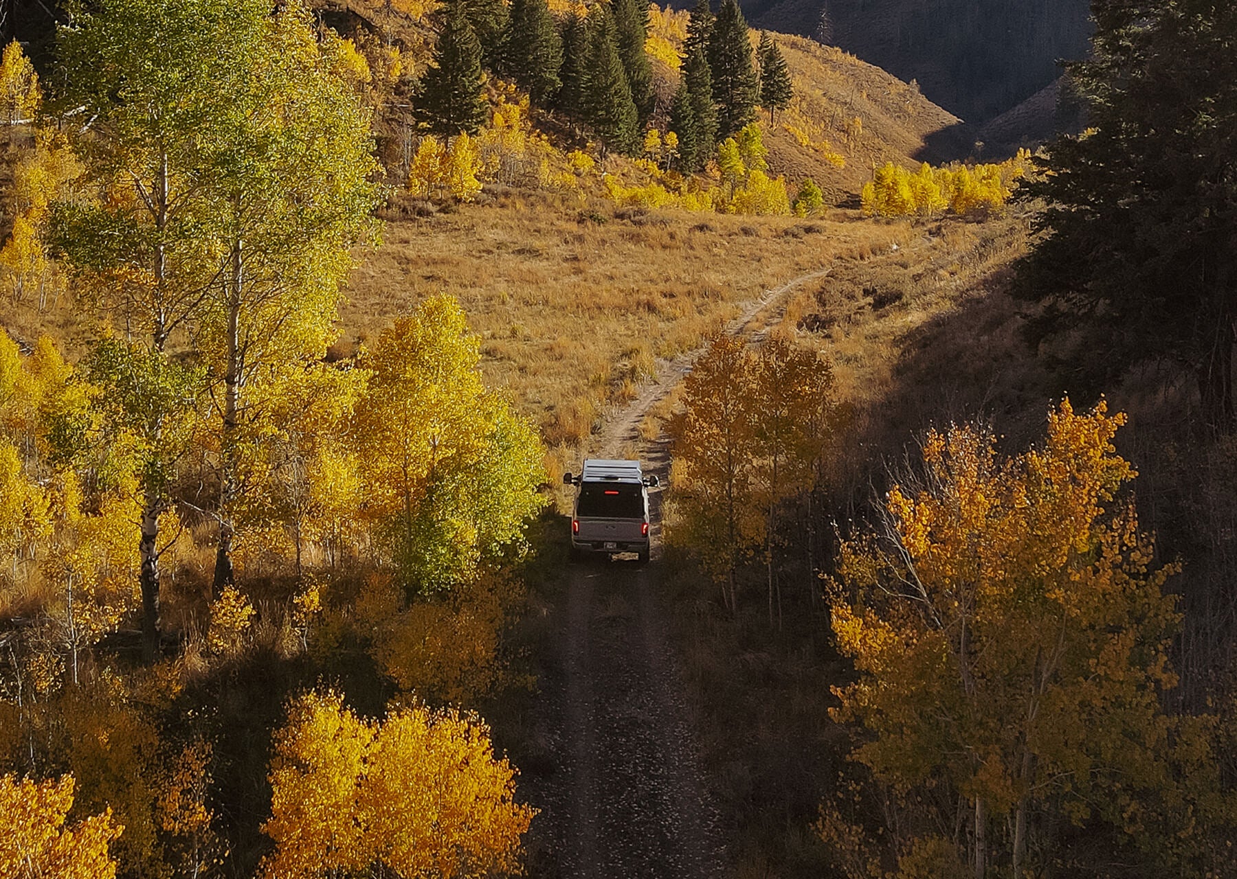 Truck driving on a dirt road through a scenic landscape with autumn trees.