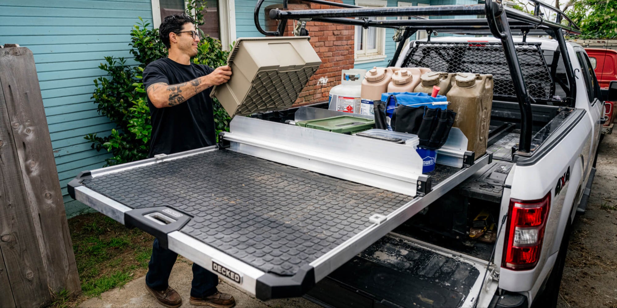 A man pulling his DECKED storage cases off of the tray of his CargoGlide at a job site. The tray of his CargoGlide is organized by CargoGlide Crossbars and Dividers. These accessories keep gear from moving around on top of his CargoGlide.