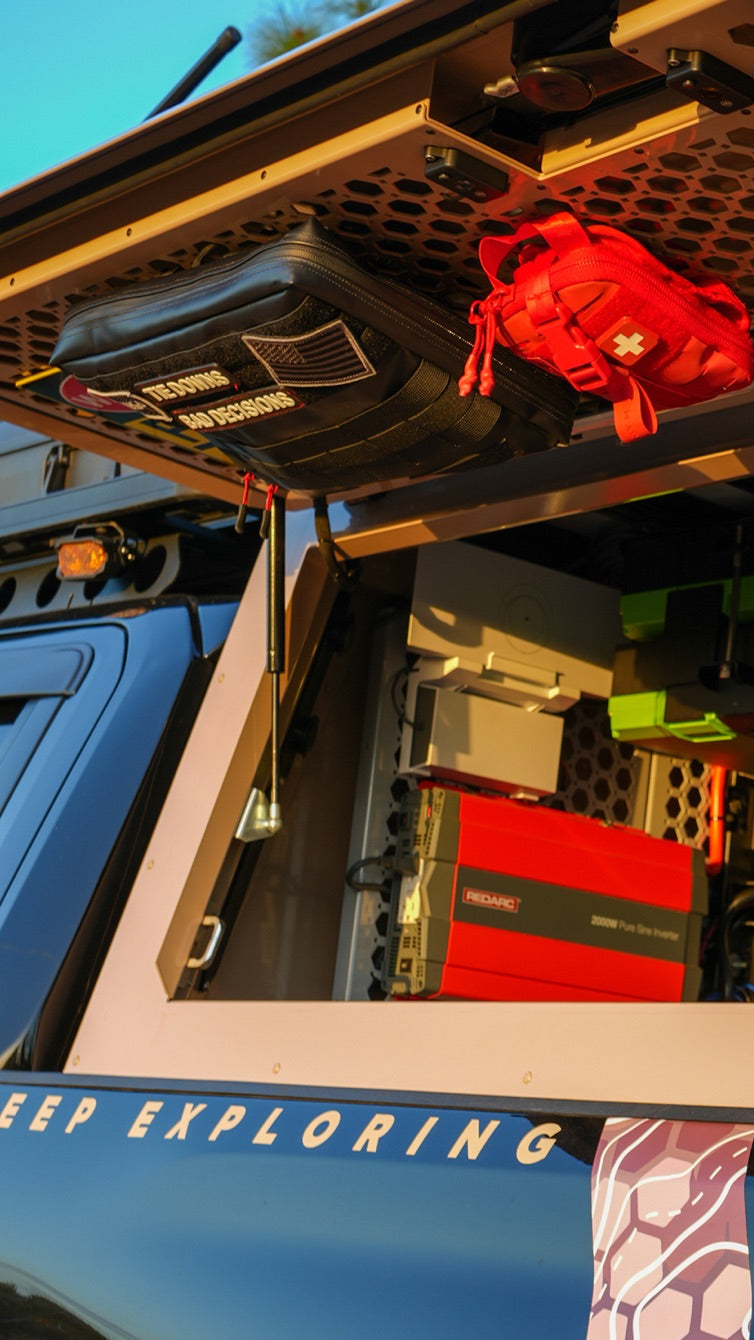 Open truck canopy with an overhead mesh storage panel holding a recovery bag and first aid kit, plus organized power equipment and storage boxes inside.