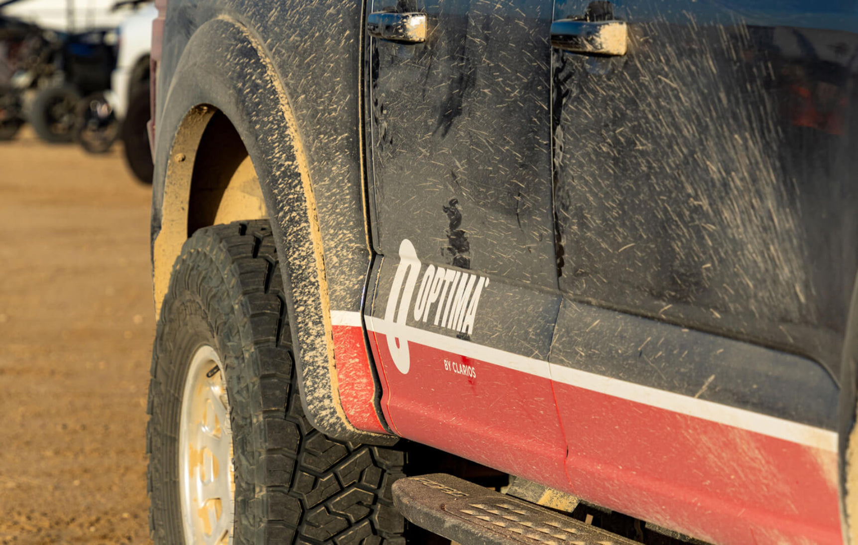 Close-up of a vehicle with 'TR Optima' branding on a dirt surface