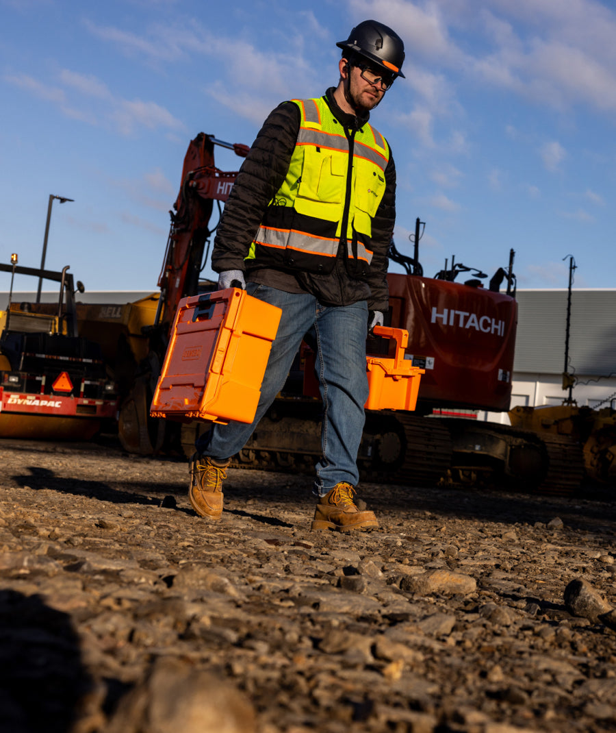 A man carrying his Blaze Orange D-co cases through a construction site.