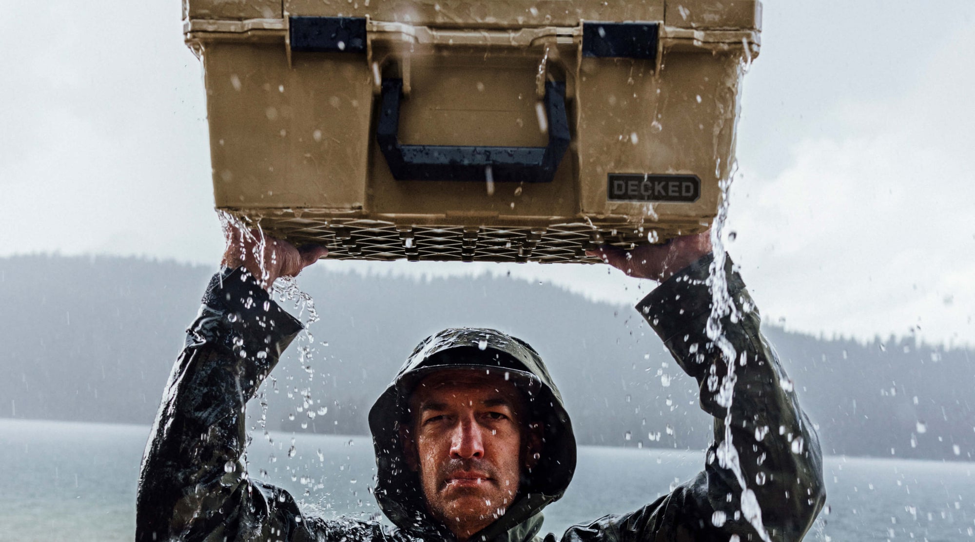A man in a rain jacket holding a Halfrack above his head. Both the case and the man are being drenched by water.