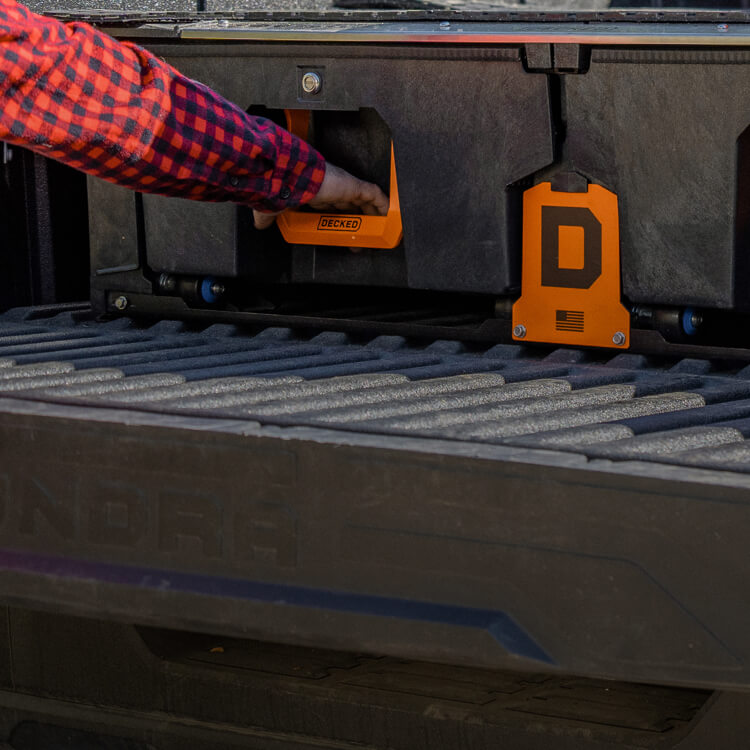 Person opening a DECKED Drawer System in a truck bed with bright orange handles.