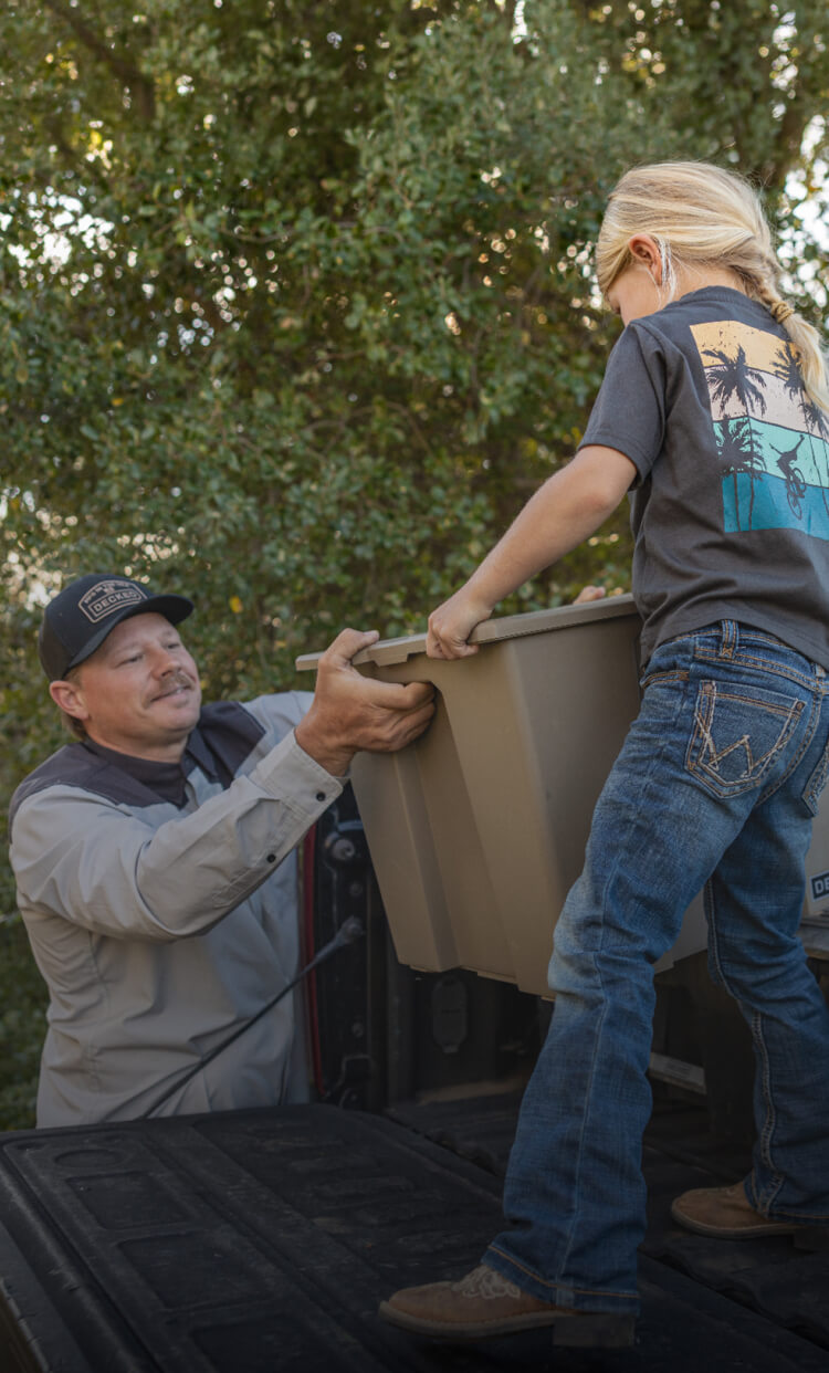 A dad and his daughter unloading the back of his truck of camping supplies for their weekend excursion.