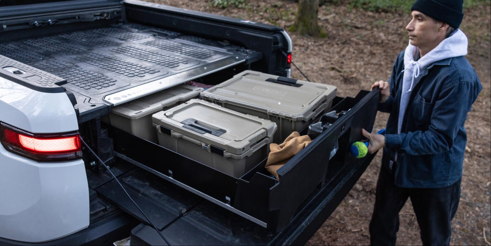 A man retrieving gear from his Rivian Drawer System to play fetch with his dog.