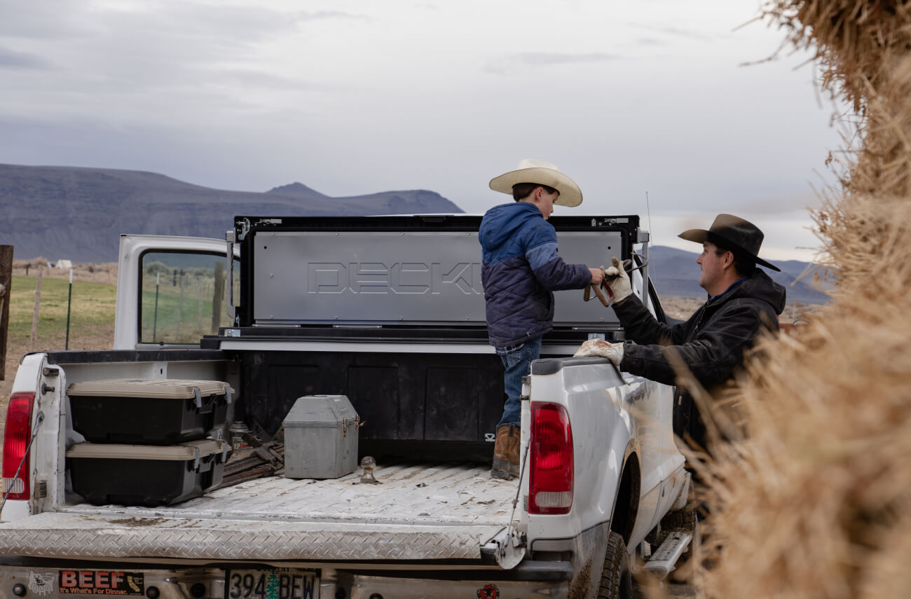 Dad handing farm tools to his son in the back of a truck