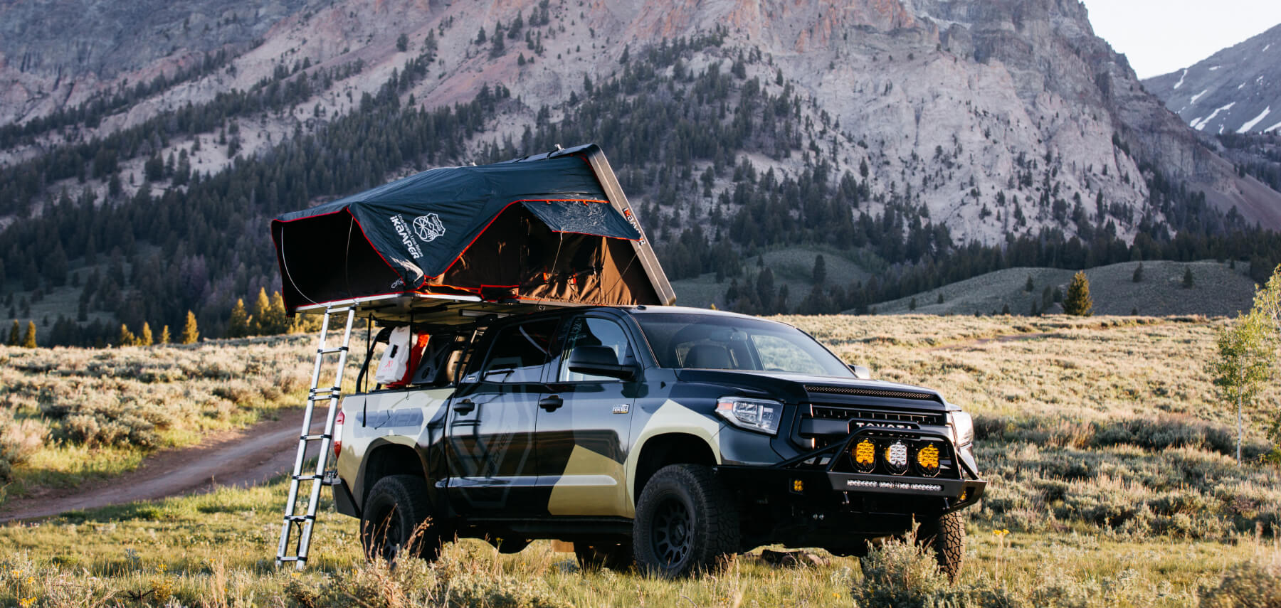 Truck in the mountains with a pickup truck tent open for camping