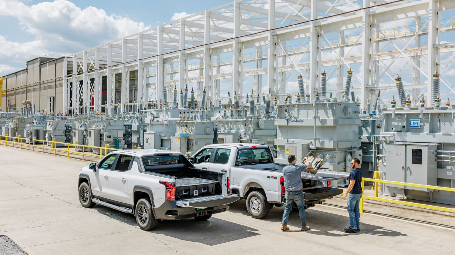 Two pickup trucks with open beds in front of a large industrial building.