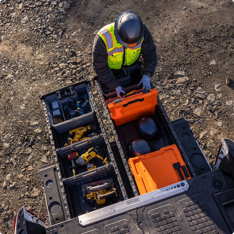 Person in high-visibility gear opening a DECKED Drawer System filled with various tools on a construction site.