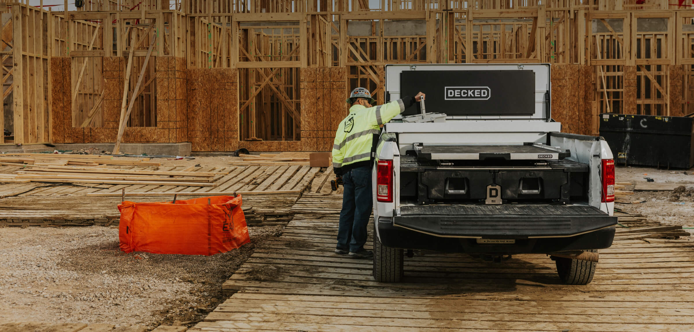 Person standing next to a truck with a 'DECKED' Tool Box, Drawer System, and CargoGlide at a construction site.