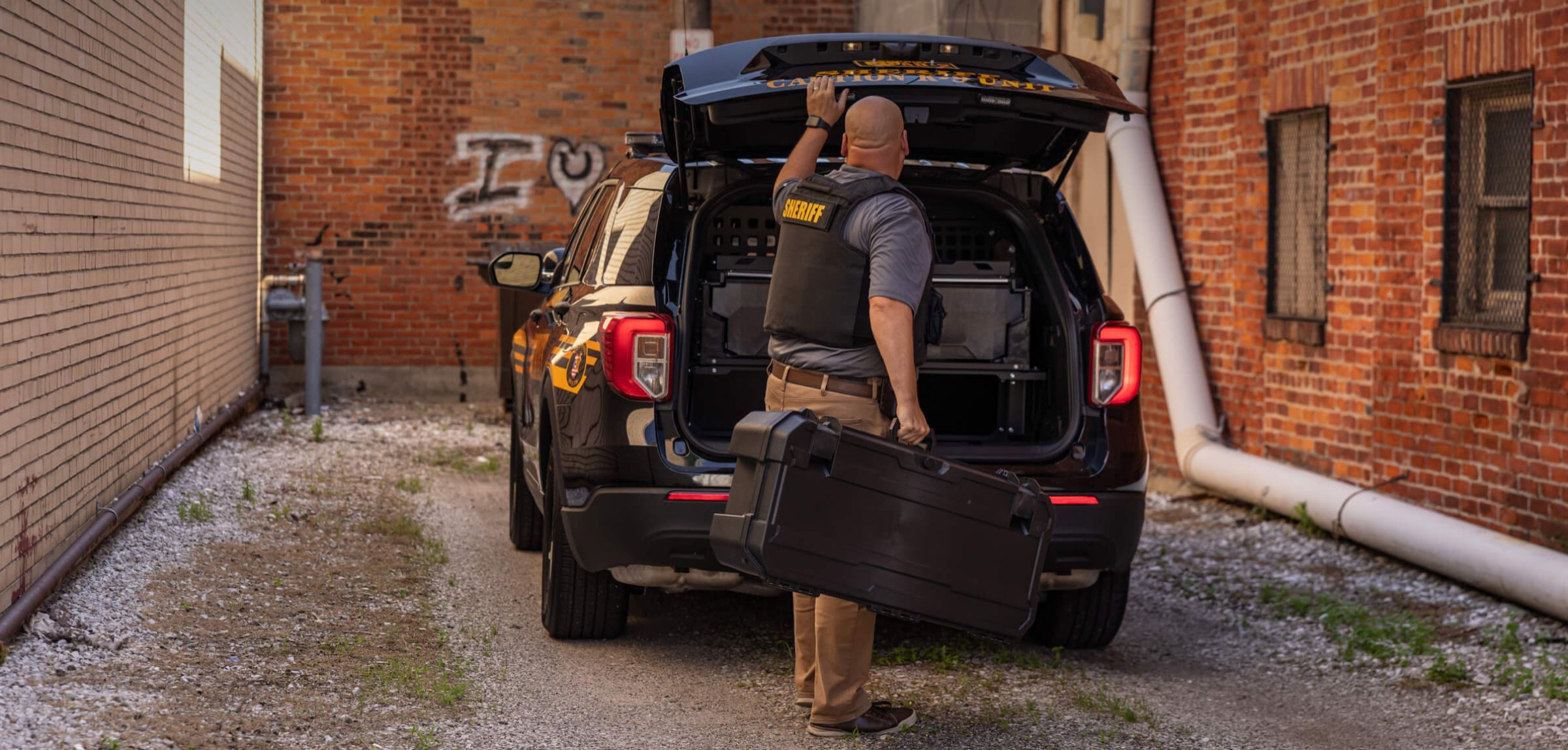 Person loading a Honcho 80 protective case into the trunk of a police car in an alleyway.